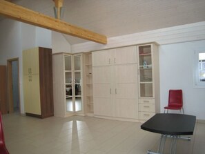 A room with a large wardrobe, a dining table, and a red chair.