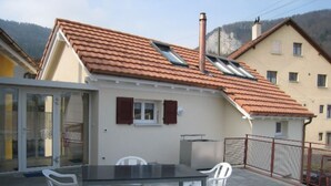 En boligbygning med et tegltag, en balkon med bord og stole, og udsigt over det omkringliggende område.