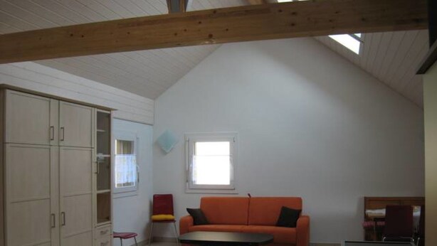 Et loftstudie med skrå vægge, en sofa, en lænestol, et lille bord og indbyggede skabe.