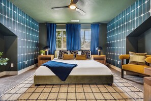Ein Schlafzimmer mit einem großen Bett, einem Deckenventilator, einem Fenster mit Vorhängen und einem Sessel.