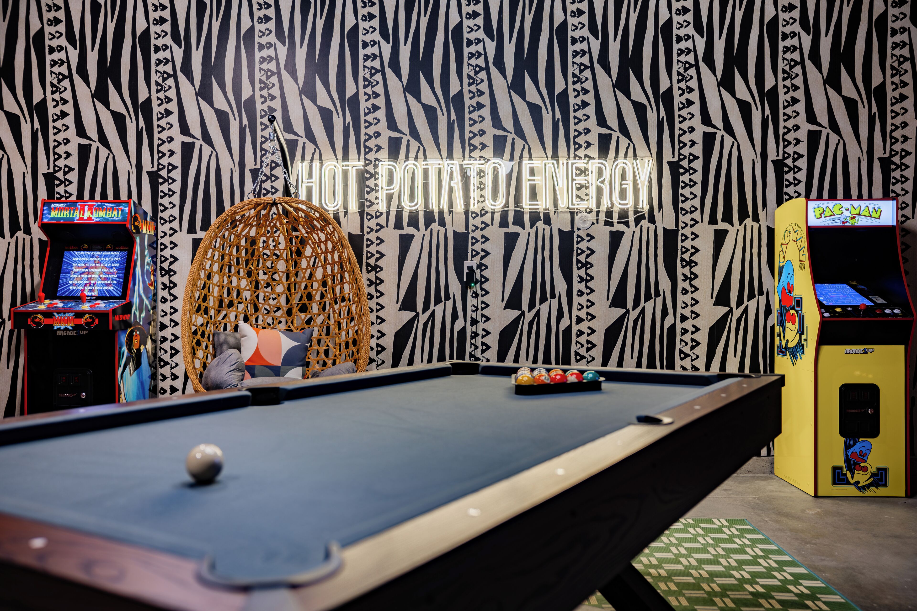 A pool table in a room with arcade machines and a hanging chair.