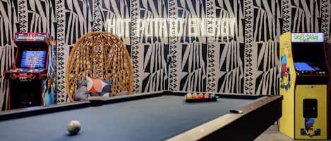 A pool table in a room with arcade machines and a hanging chair.