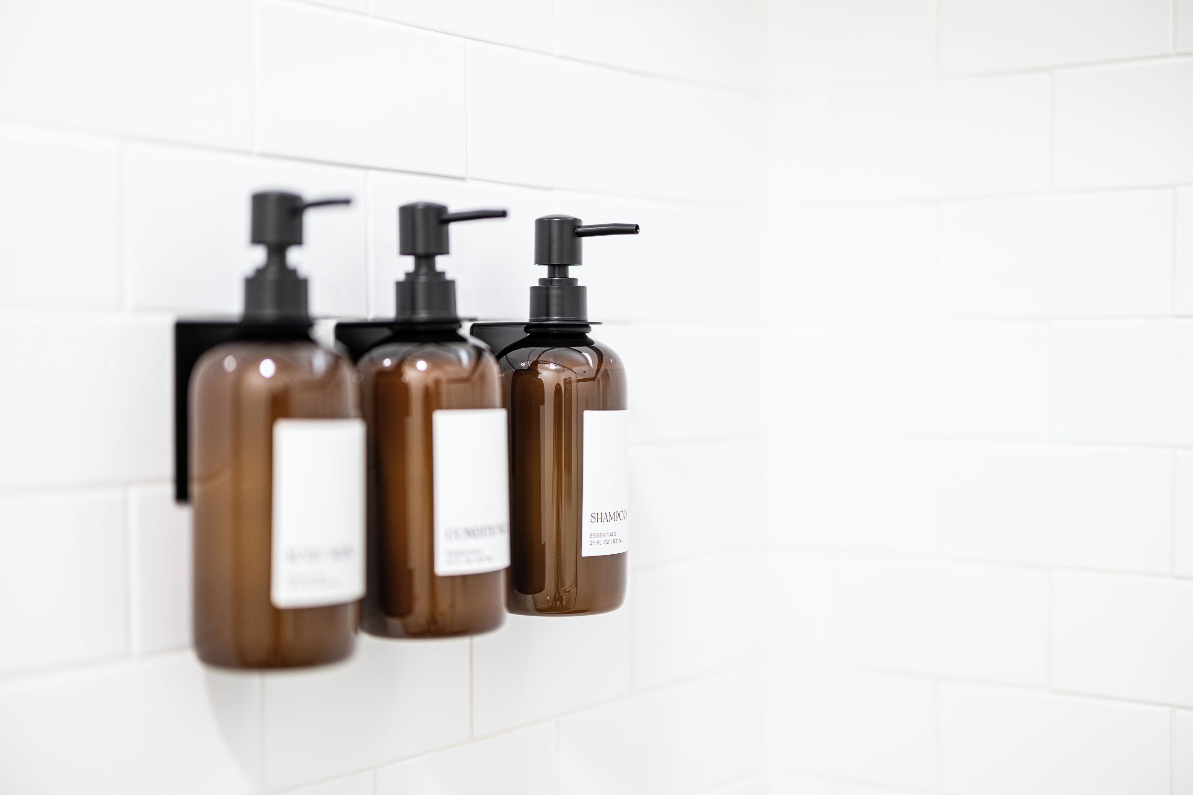 Trois bouteilles marron, dotées de pompes noires, sont fixées à un mur recouvert de carreaux blancs.