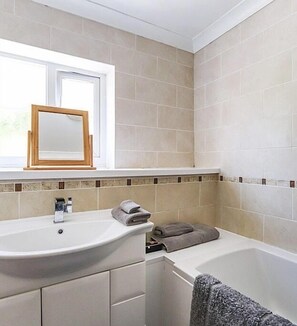 Un baño con lavamanos blanco, un espejo encima y una bañera.