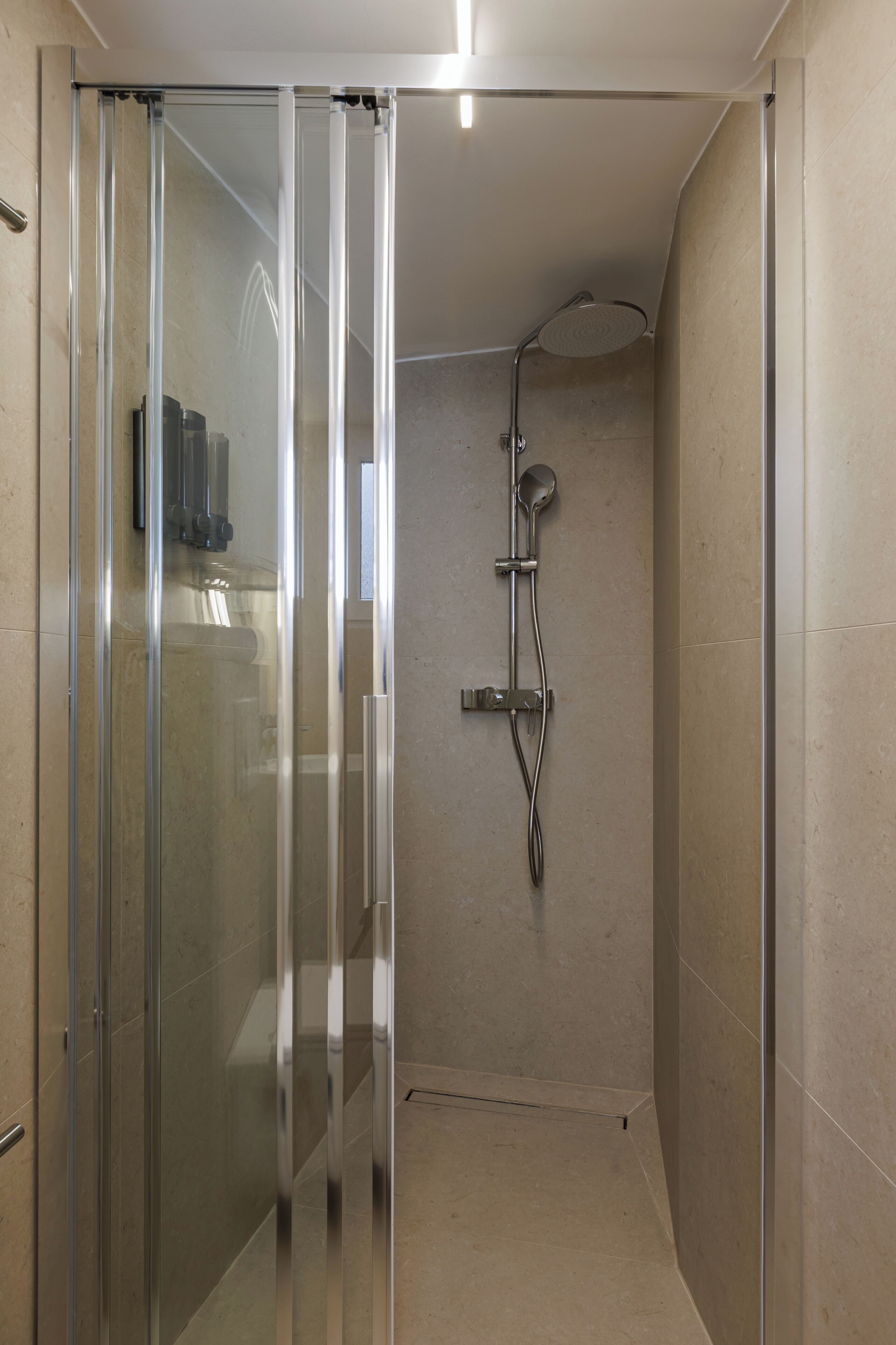A modern shower with a glass door, a handheld showerhead, and a wall-mounted faucet.