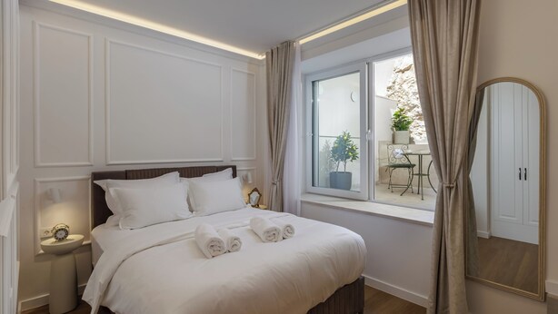 Hotellihuone, jossa on sänky, yöpöydät, ikkuna verhoilla, ruukkukasvi ja peili.