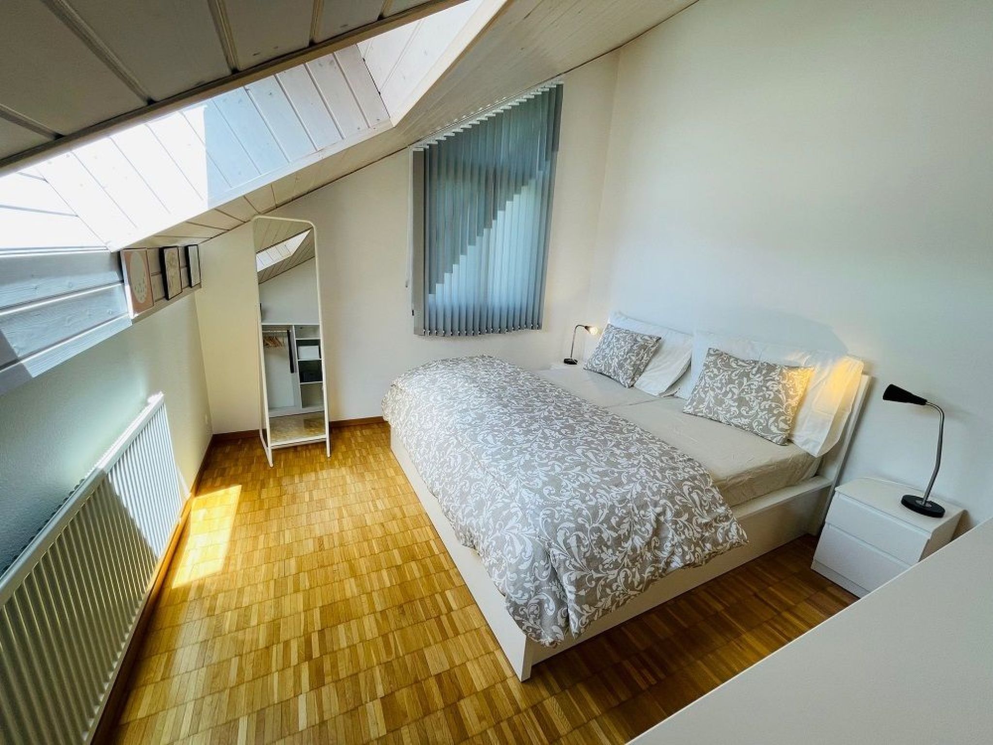 Une chambre à coucher comprenant un lit, des tables de chevet, une armoire et une fenêtre avec des stores.