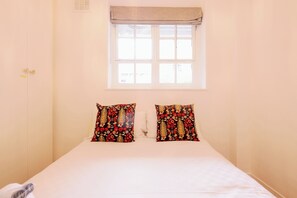 A bedroom with a single bed, a window with a blind, and two decorative pillows. - Stylish 1-Bed in Bethnal Green • Calm & Central - Pass the Keys (London)