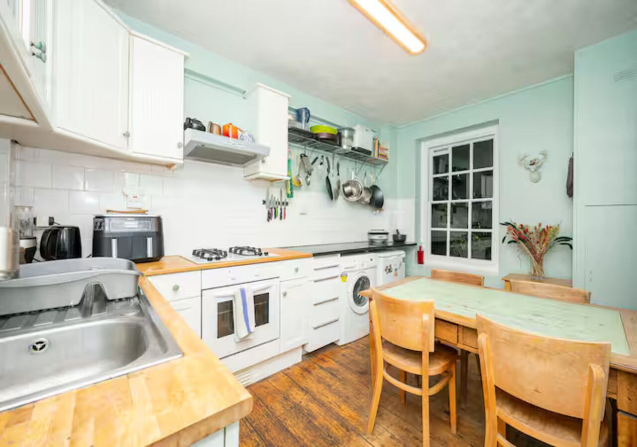 Une cuisine avec des meubles blancs, un plan de travail en bois, un évier, une cuisinière et une table à manger avec des chaises.