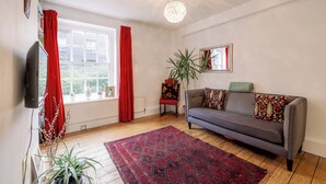 A living room with a sofa, a red rug, a television, and a window with curtains. - Stylish 1-Bed in Bethnal Green • Calm & Central - Pass the Keys (London)