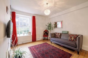A living room with a sofa, a red rug, a television, and a window with curtains. - Stylish 1-Bed in Bethnal Green • Calm & Central - Pass the Keys (London)