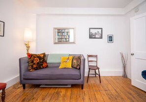 A room with a grey sofa, a wooden chair, a bookshelf, and a door. - Stylish 1-Bed in Bethnal Green • Calm & Central - Pass the Keys (London)