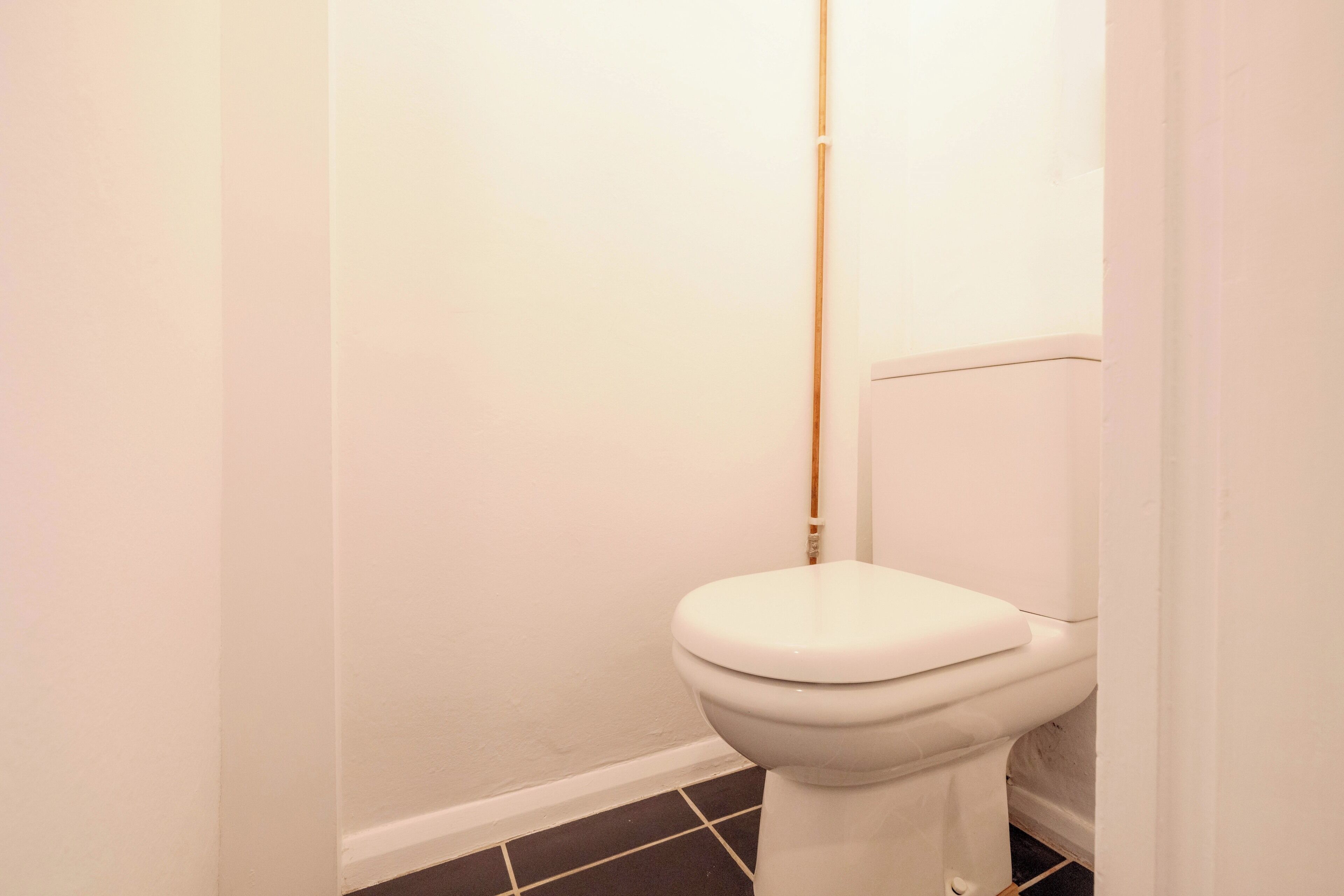 Des toilettes blanches avec une chasse d’eau, un porte-rouleau en bois et un sol carrelé.