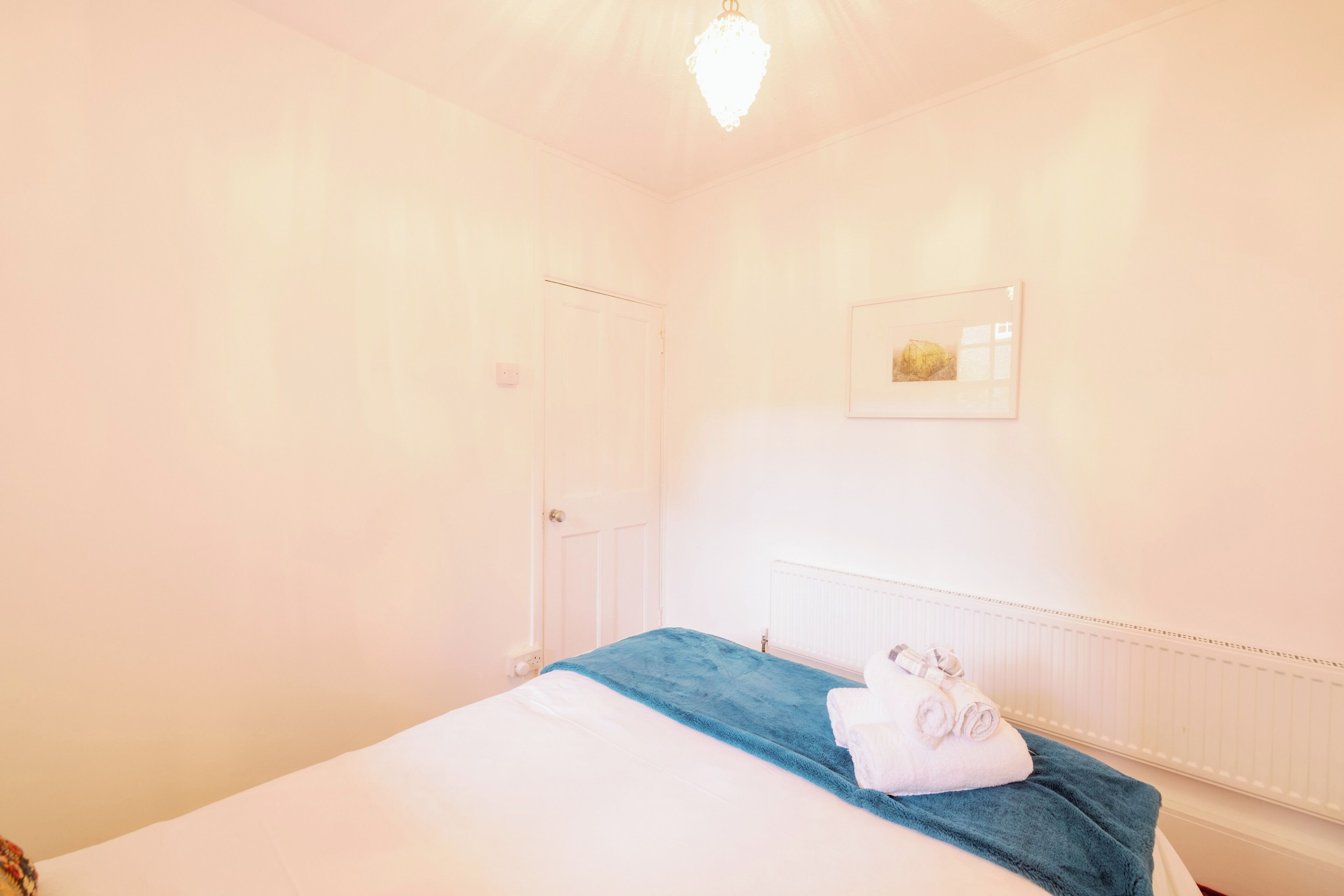 A hotel room with a bed, a radiator, a door, and a framed picture on the wall.