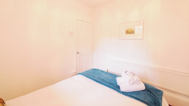 A hotel room with a bed, a radiator, a door, and a framed picture on the wall. - Stylish 1-Bed in Bethnal Green • Calm & Central - Pass the Keys (London)