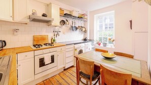 A kitchen with white cabinets, a gas stove, a wooden countertop, and a window with a view of greenery. - Stylish 1-Bed in Bethnal Green • Calm & Central - Pass the Keys (London)