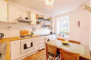 A kitchen with white cabinets, a gas stove, a wooden countertop, and a window with a view of greenery. - Stylish 1-Bed in Bethnal Green • Calm & Central - Pass the Keys (London)