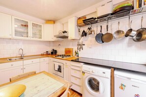 Eine Küche mit weißen Schränken, einem Holztisch, einer eingebauten Waschmaschine und hängenden Töpfen.