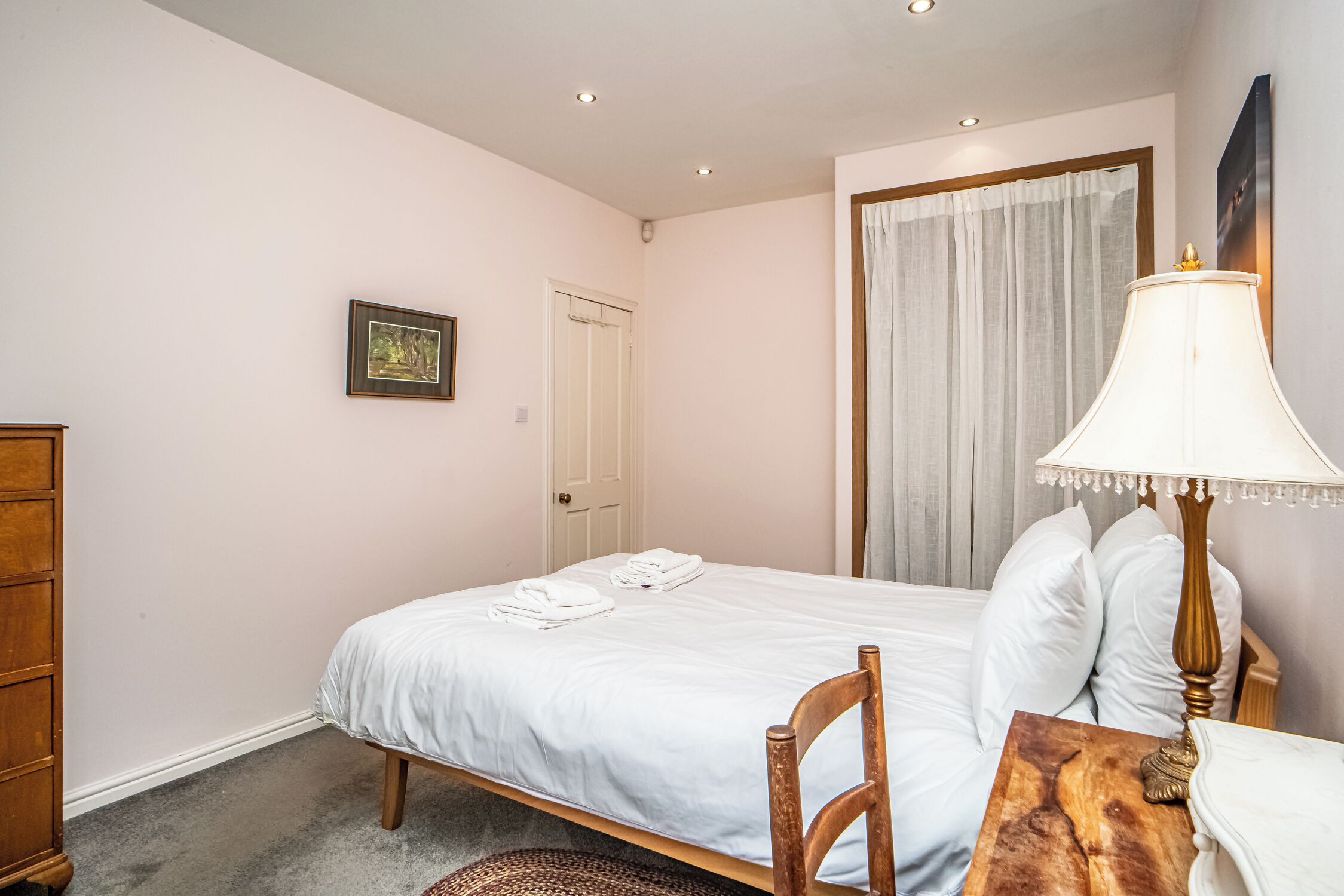 Un dormitorio con una cama individual, una mesita de noche de madera, una lámpara, un cuadro en la pared y una puerta.