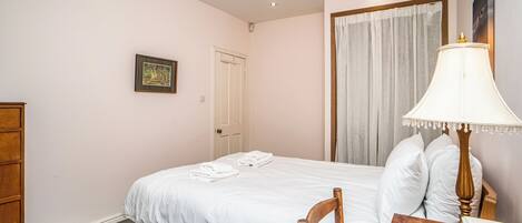 Un dormitorio con una cama individual, una mesita de noche de madera, una lámpara, un cuadro en la pared y una puerta.