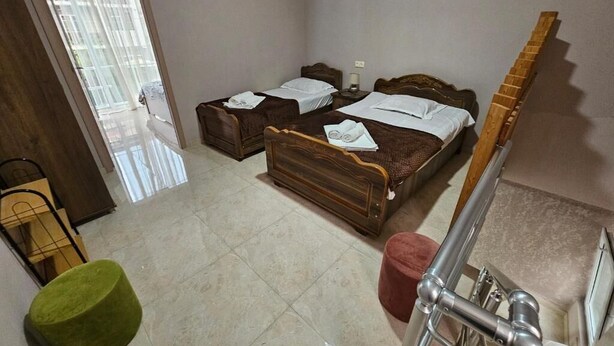Una habitación con dos camas, un reposapiés verde, un taburete rojo y una escalera de madera.
