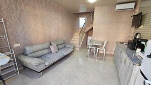 Una sala de estar con un sofá, una mesa de comedor y una zona de cocina con armarios y electrodomésticos.