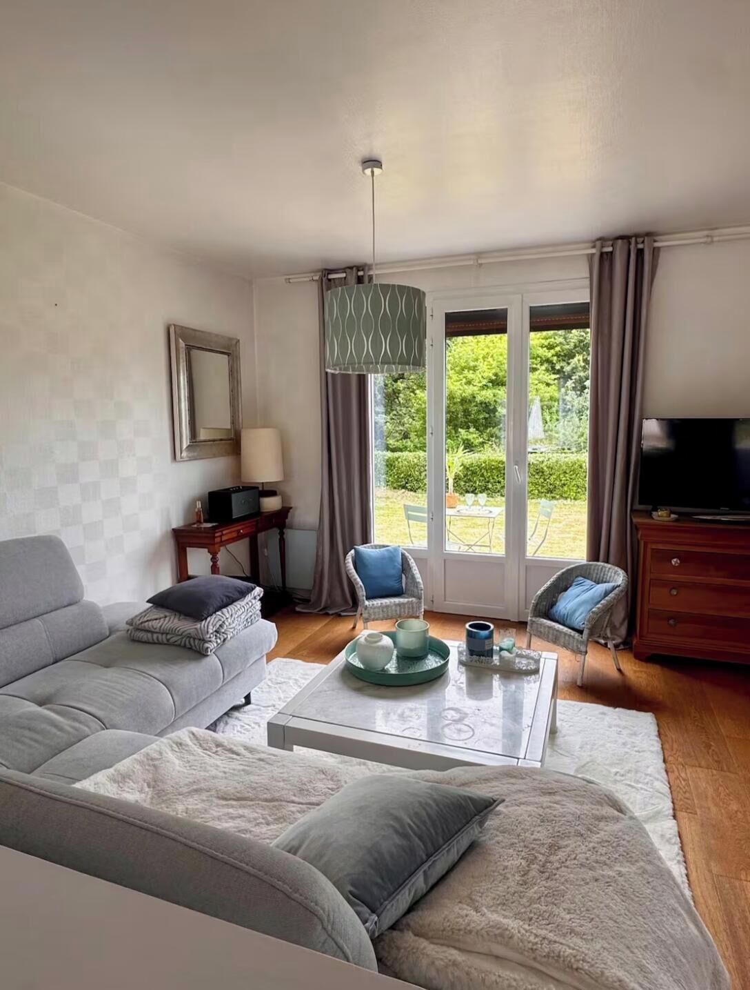 A living room with a sofa, chairs, a coffee table, a television, and a view of greenery outside.