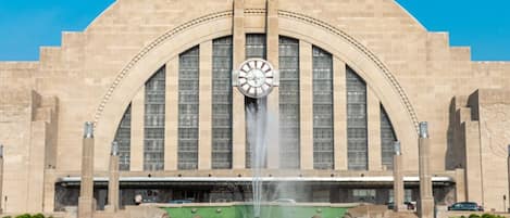 A large building with a prominent clock tower and a fountain in front.
