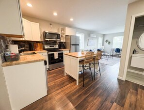 A modern kitchen with white cabinetry, stainless steel appliances, and a wooden dining table with chairs. - Contemporary 1 BR Near Xavier & Downtown w/Parking (Cincinnati)