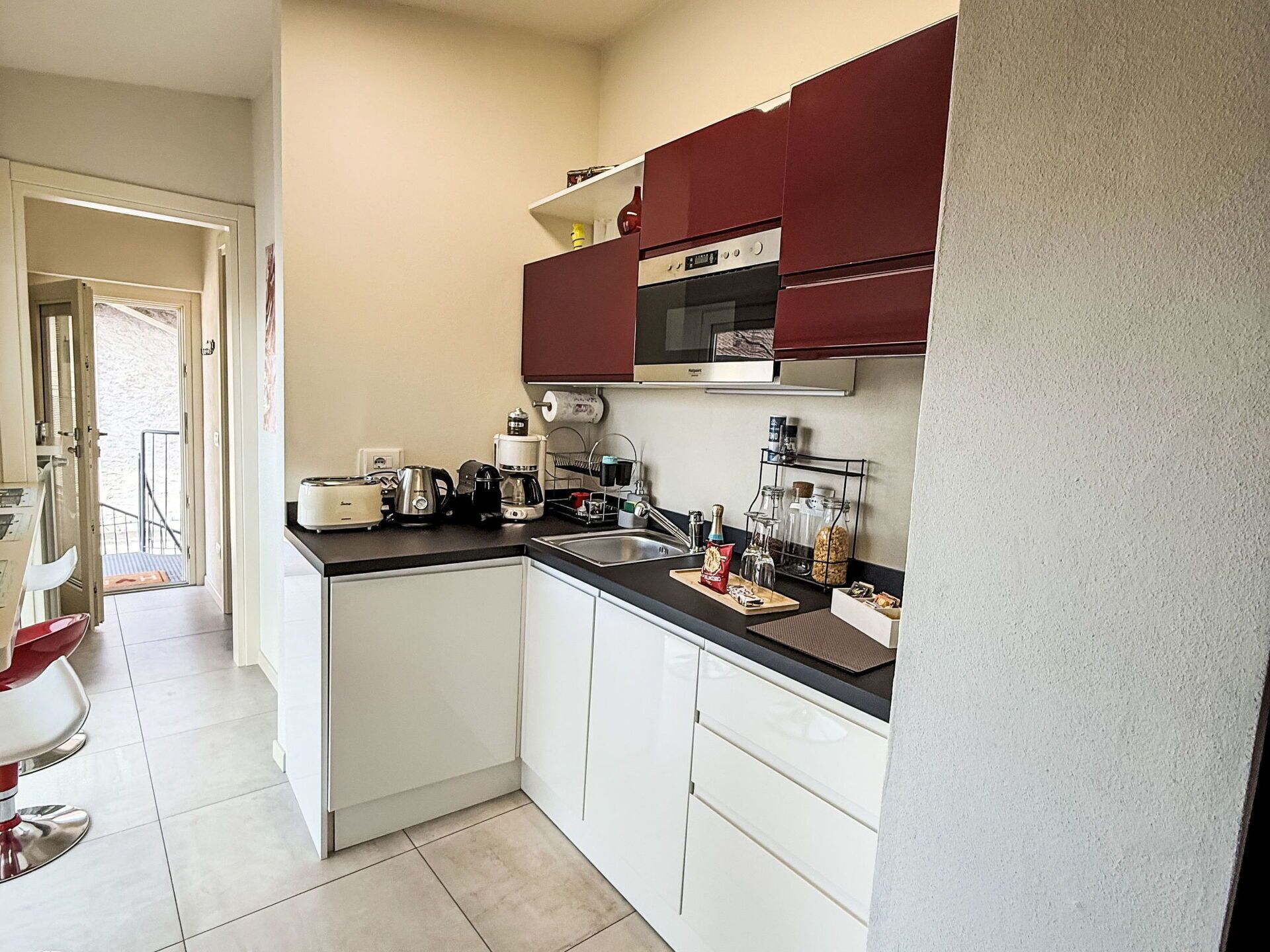 Een kleine keuken met witte kastjes, een zwart aanrecht en een rode achterwand.