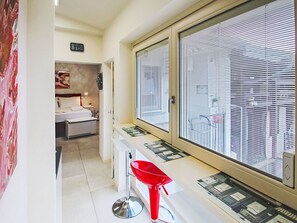 A hotel room with a bed, a red chair, a window with blinds, and a wall clock. - Beautiful apartment for 3 people with WIFI, A/C, TV and balcony (Colazza)