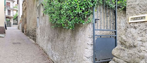 A narrow cobblestone street with a stone wall on one side and a metal gate on the other.