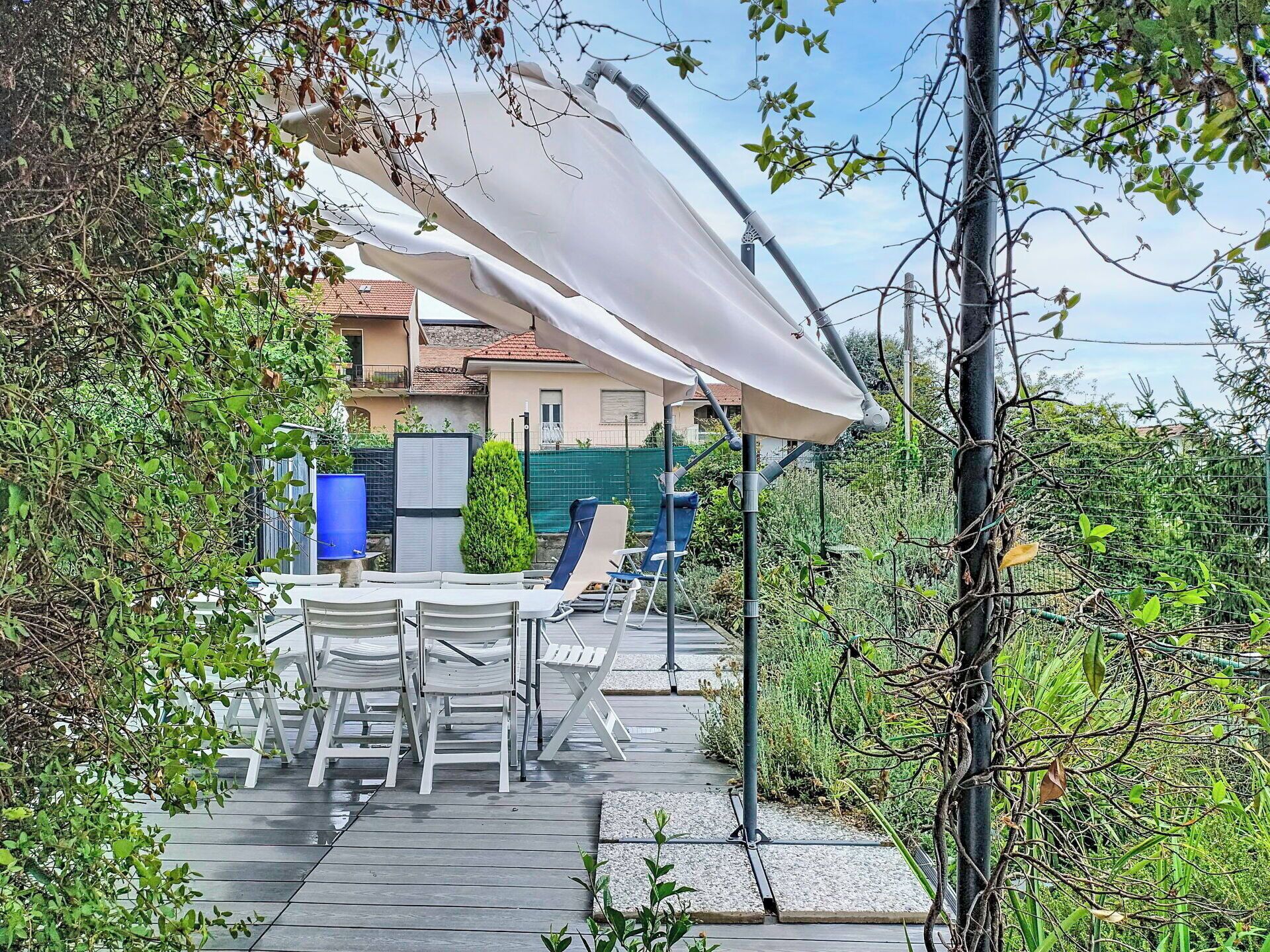 Eine Terrasse im Freien mit Tisch und Stühlen, umgeben von viel Grün und einem Haus im Hintergrund.