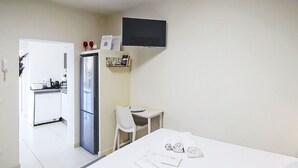 A small, clean room with a bed, a desk, a chair, a refrigerator, and a television mounted on the wall. - Beautiful apartment for 3 guests with WIFI, A/C, TV and balcony (Colazza)