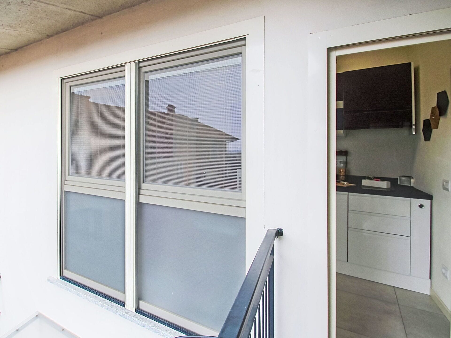 A room with a large window, a kitchen area with cabinets, and a door leading to another room.
