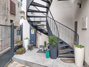 Eine Wendeltreppe führt zu einer oberen Etage, umgeben von Topfpflanzen und einem Metallgitter.