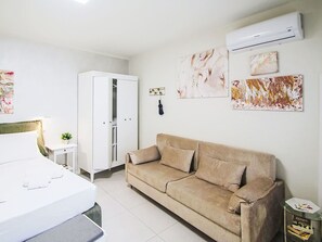 Ein modernes Schlafzimmer mit einem Bett, einem weißen Kleiderschrank, einem beigen Sofa und einem kleinen Nachttisch.