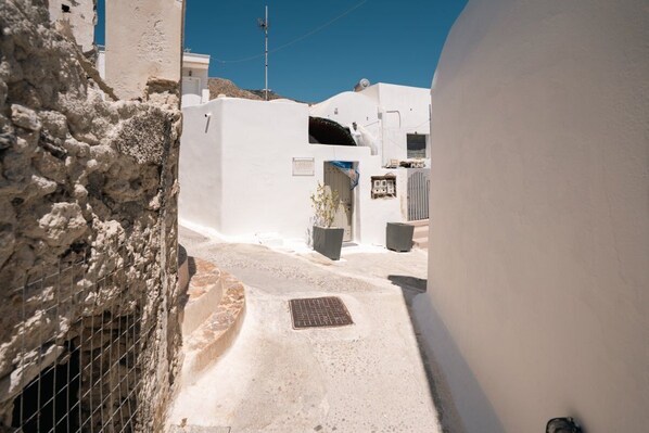 Une rue étroite bordée de bâtiments blancs, avec une grille en métal et un chemin pavé.