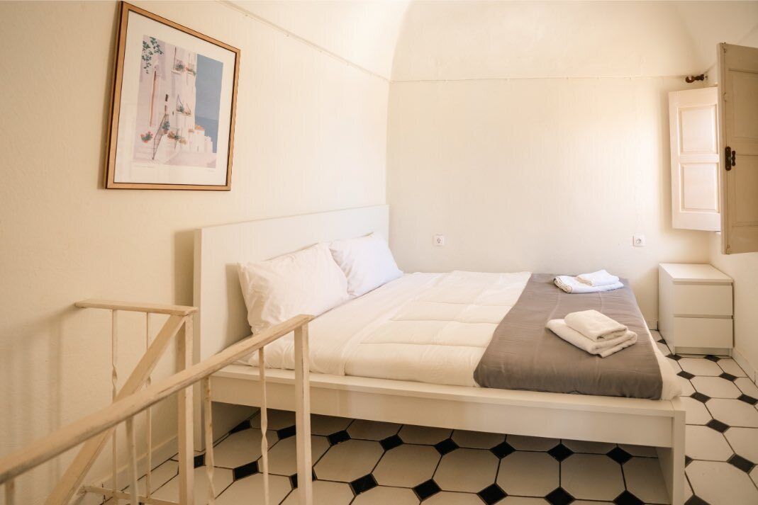 A bedroom with a bed, a bedside table, a nightstand, a framed picture on the wall, and a staircase.