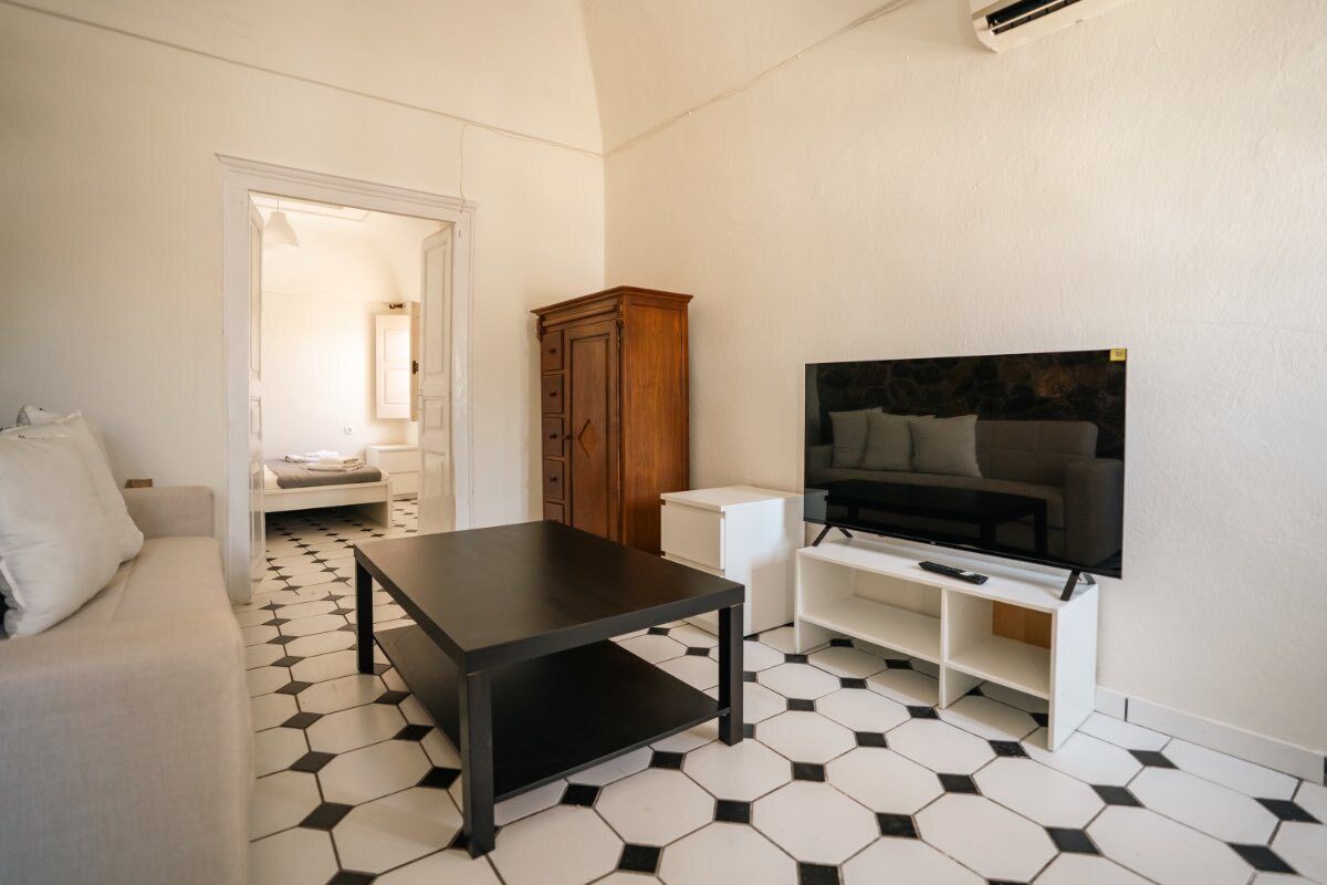 A hotel room with a sofa, a coffee table, a TV on a stand, a wardrobe, and a patterned floor.