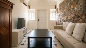 A living room with a sofa, a coffee table, a television, and a stone wall.