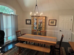 A dining room with a large wooden table, benches, a chandelier, and a glass cabinet with decorative items. - UGA GAME DAY Home w/3 bedrooms-6 People (Athens)