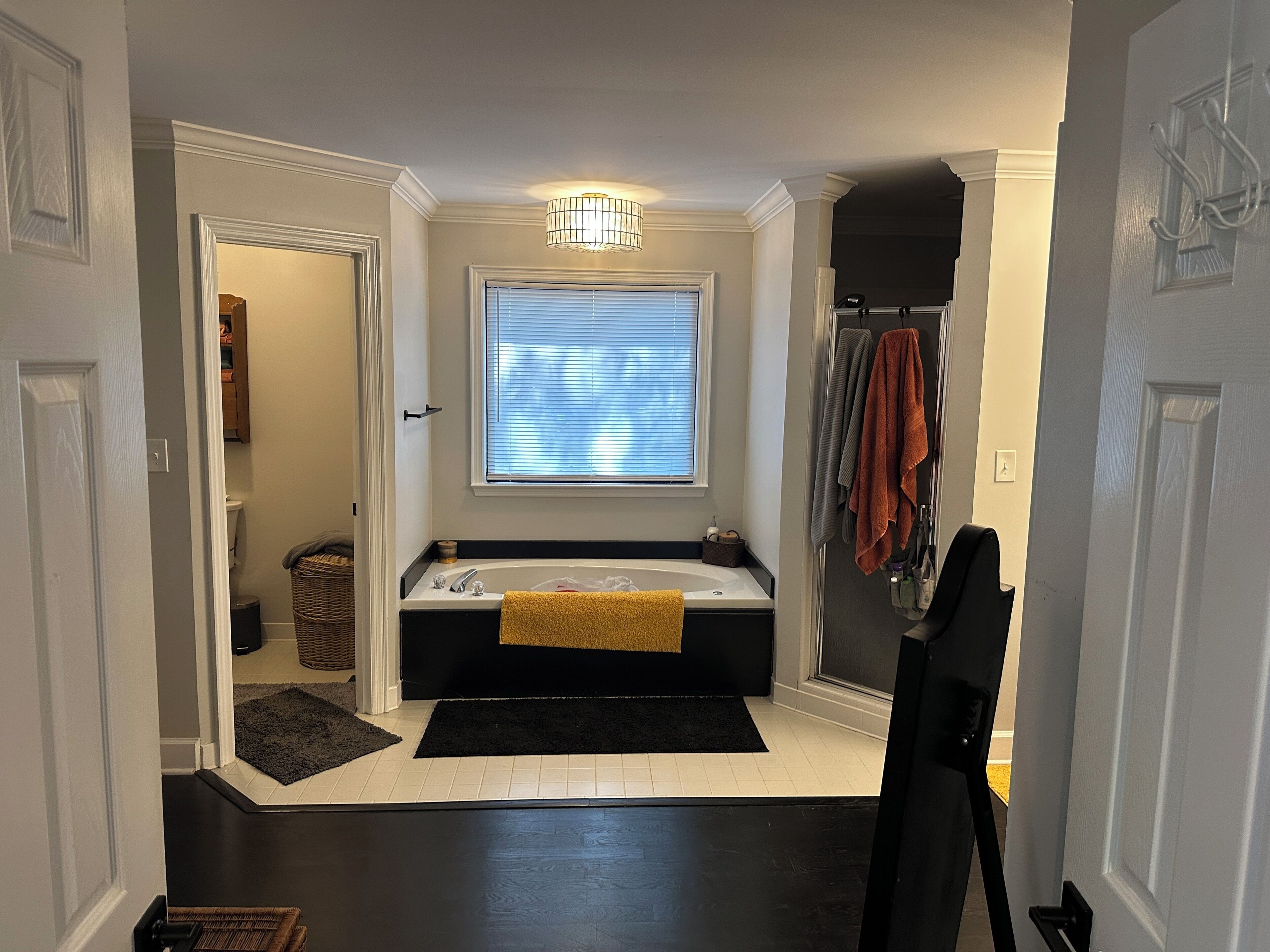A modern bathroom with a bathtub, a window with blinds, a towel rack, and a black rug.