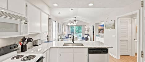 A modern kitchen with white cabinetry, a granite countertop, a built-in oven, and a dishwasher.