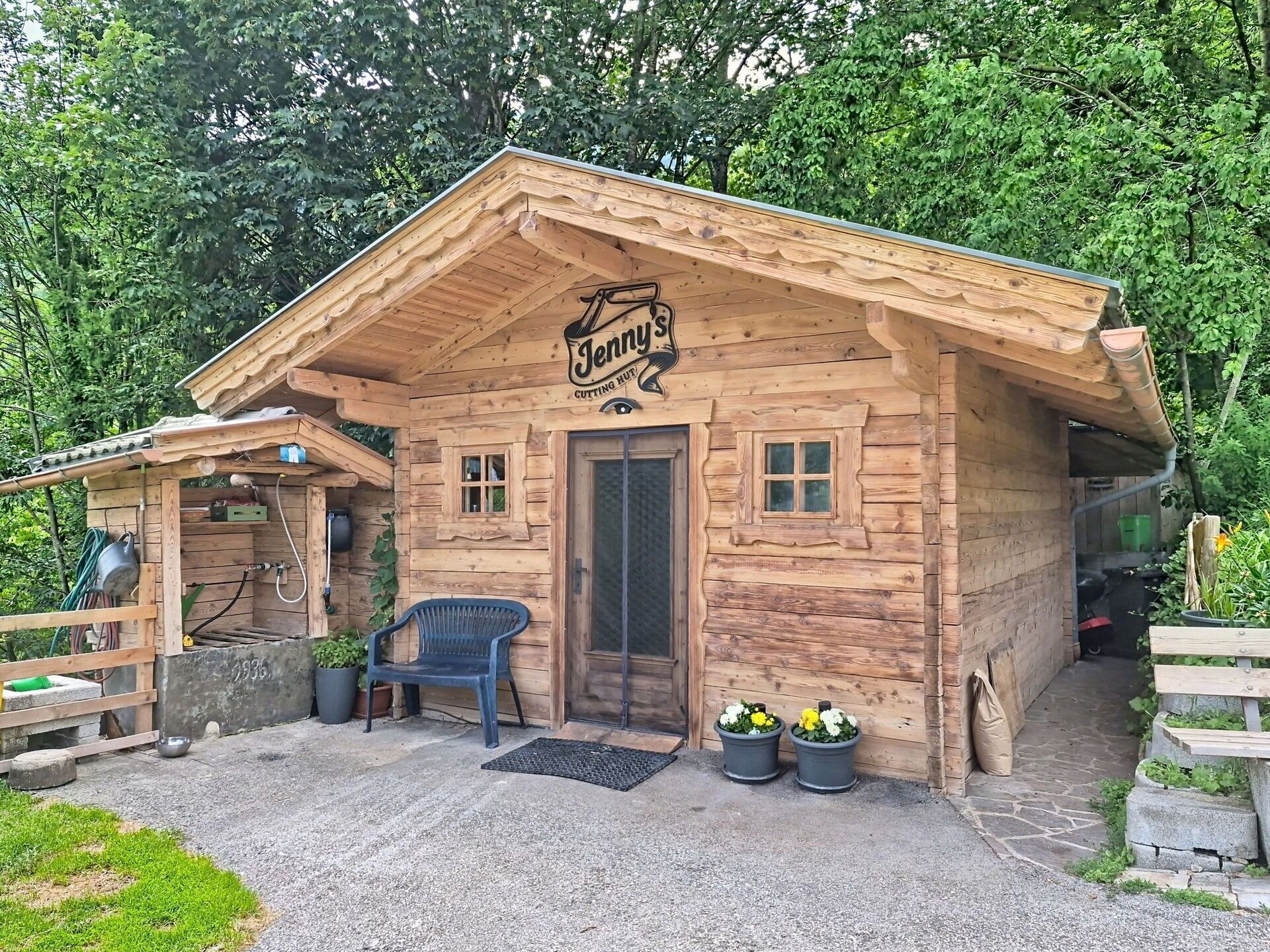 A wooden cabin with a sign reading 'Jenny's Cutting Hut' and a bench outside.