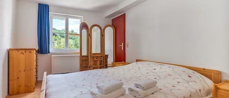 Ein Schlafzimmer mit einem Bett, einem Holzschrank, einem Fenster mit Vorhängen, einem Spiegel und einer roten Tür.
