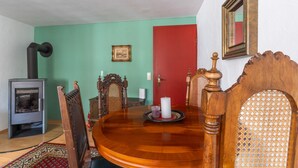 Un coin repas avec une table en bois, des chaises, une porte rouge, un tableau encadré au mur et un poêle à bois.