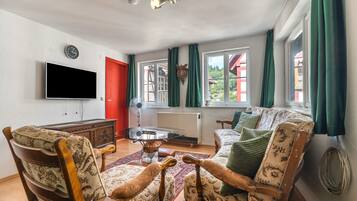 Ein Wohnzimmer mit Flachbildfernseher, Holzschrank, antiken Ventilator und einer Couch mit gemusterten Kissen.