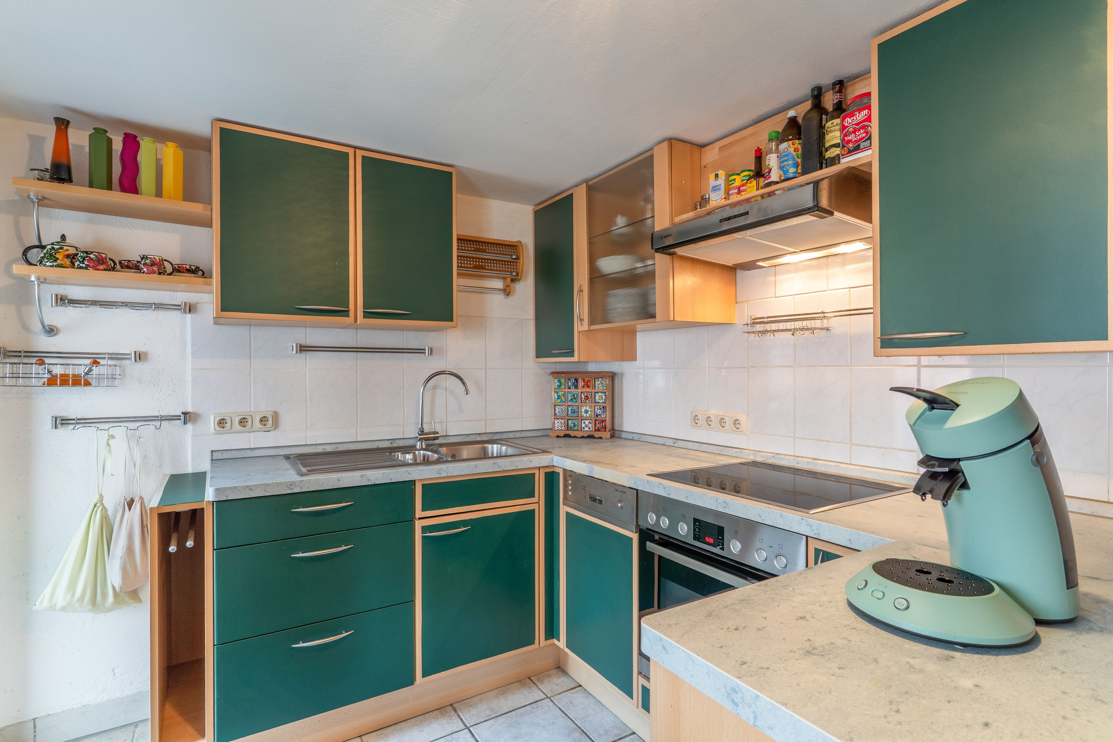 A kitchen with green cabinets, a built-in oven, a sink, and a coffee maker.