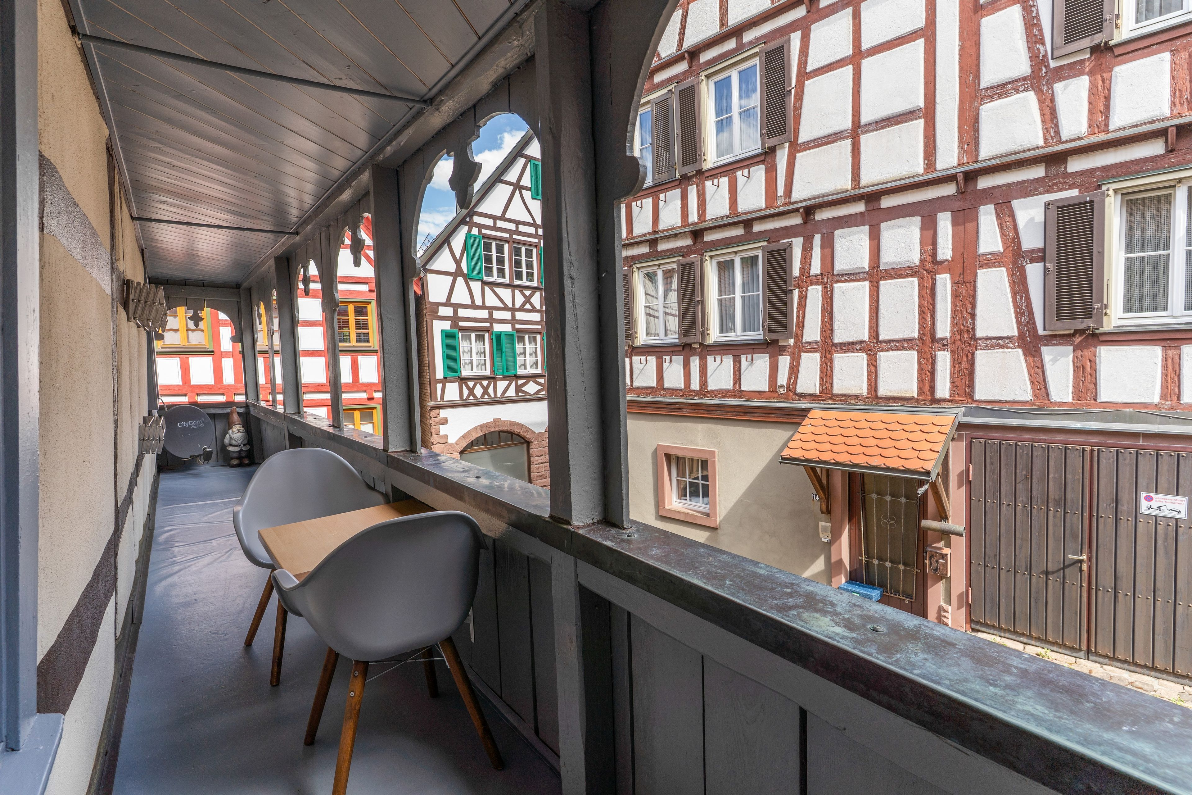 Ein Balkon mit zwei Stühlen, Blick auf traditionelle Fachwerkhäuser und ein kleines Fenster mit einer Tür.